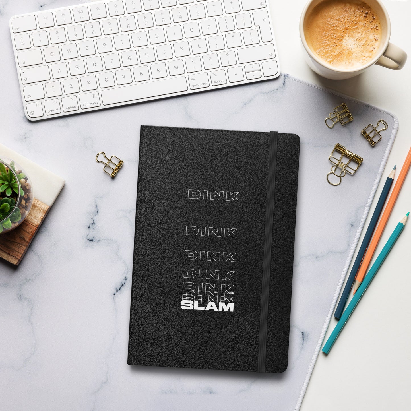 Dink Dink Slam type on black notebook, front view on marble surface with work accessories