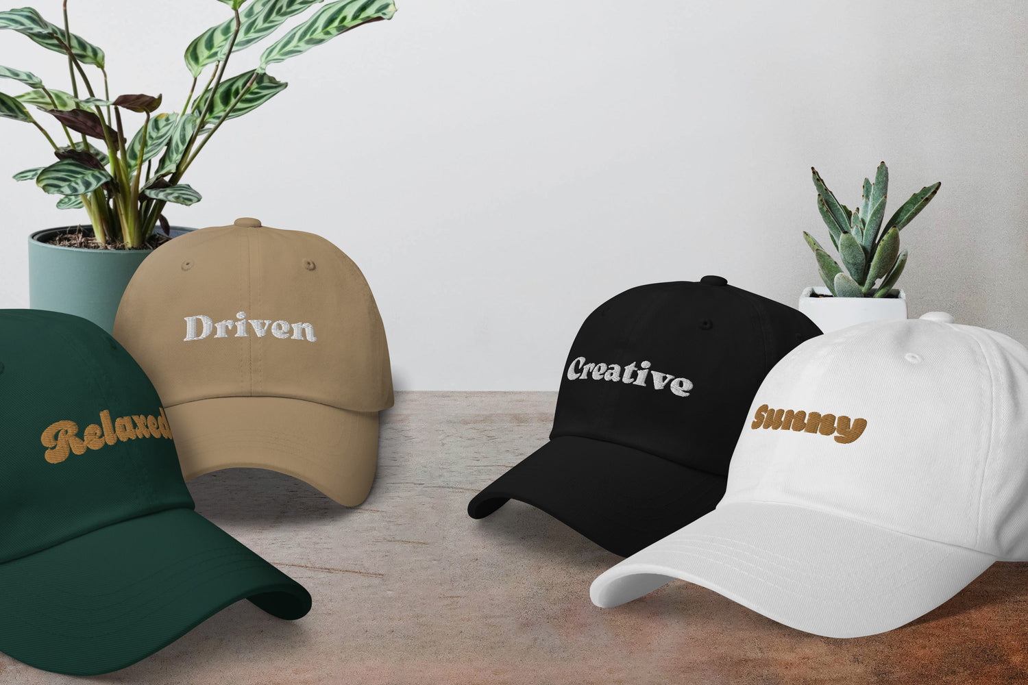 Four dad hats with embroidered type (Relaxed, Driven, Creative and Sunny) on casual background