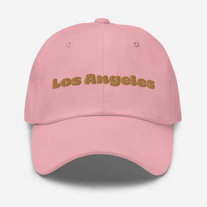 Los Angeles city editions with “Los Angeles” type in gold embroidery on pink casual dad hat front view on white background