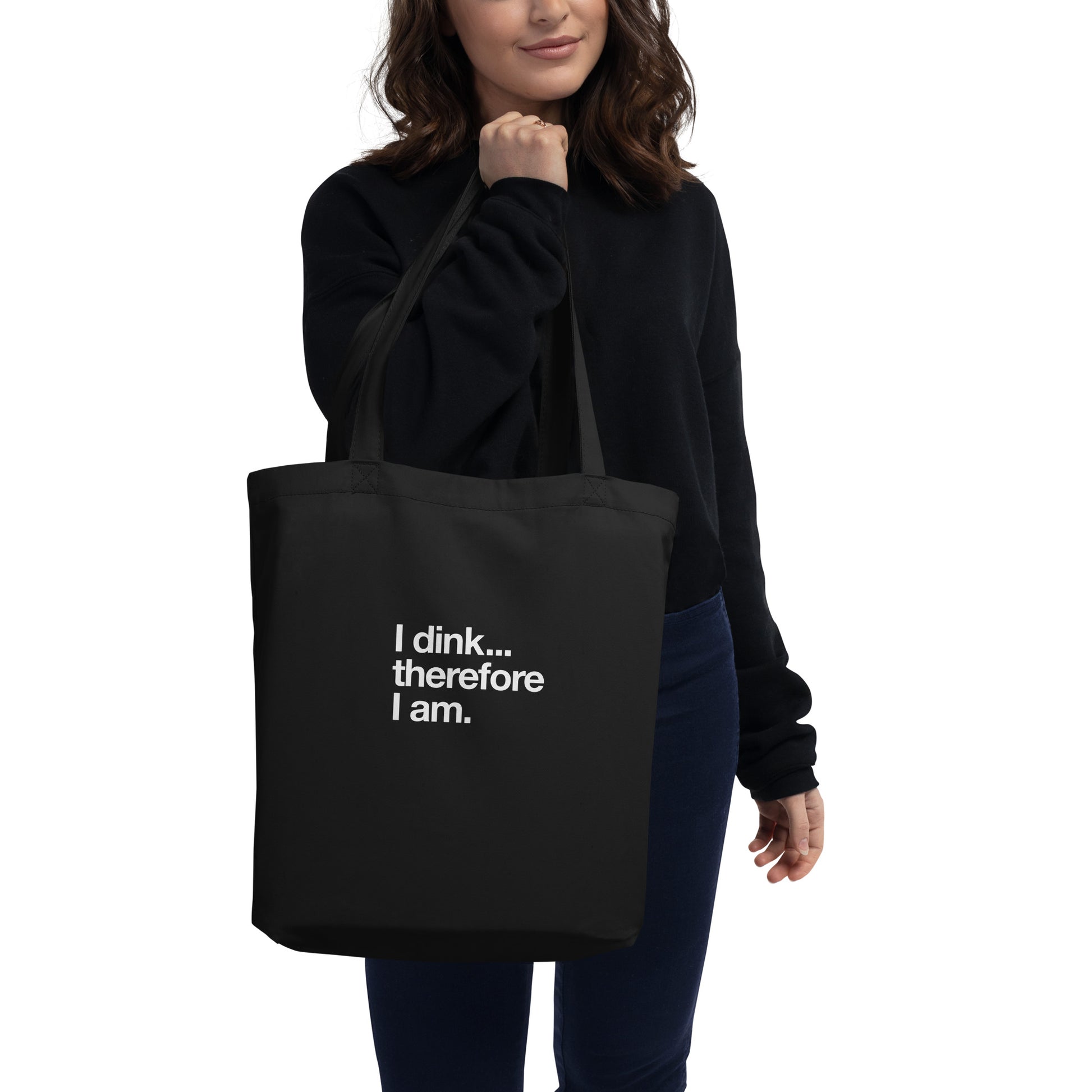 I Dink... Therefore I Am. white text on black tote bag, front view, being held by female model