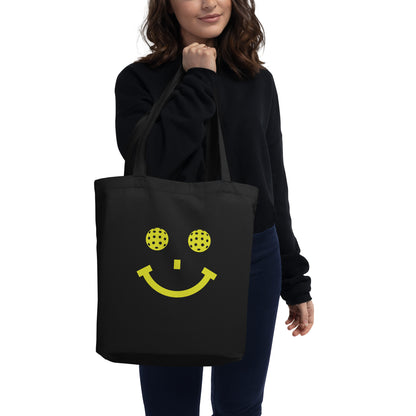 Pickleball Smile graphic on black tote bag, front view being held by female model