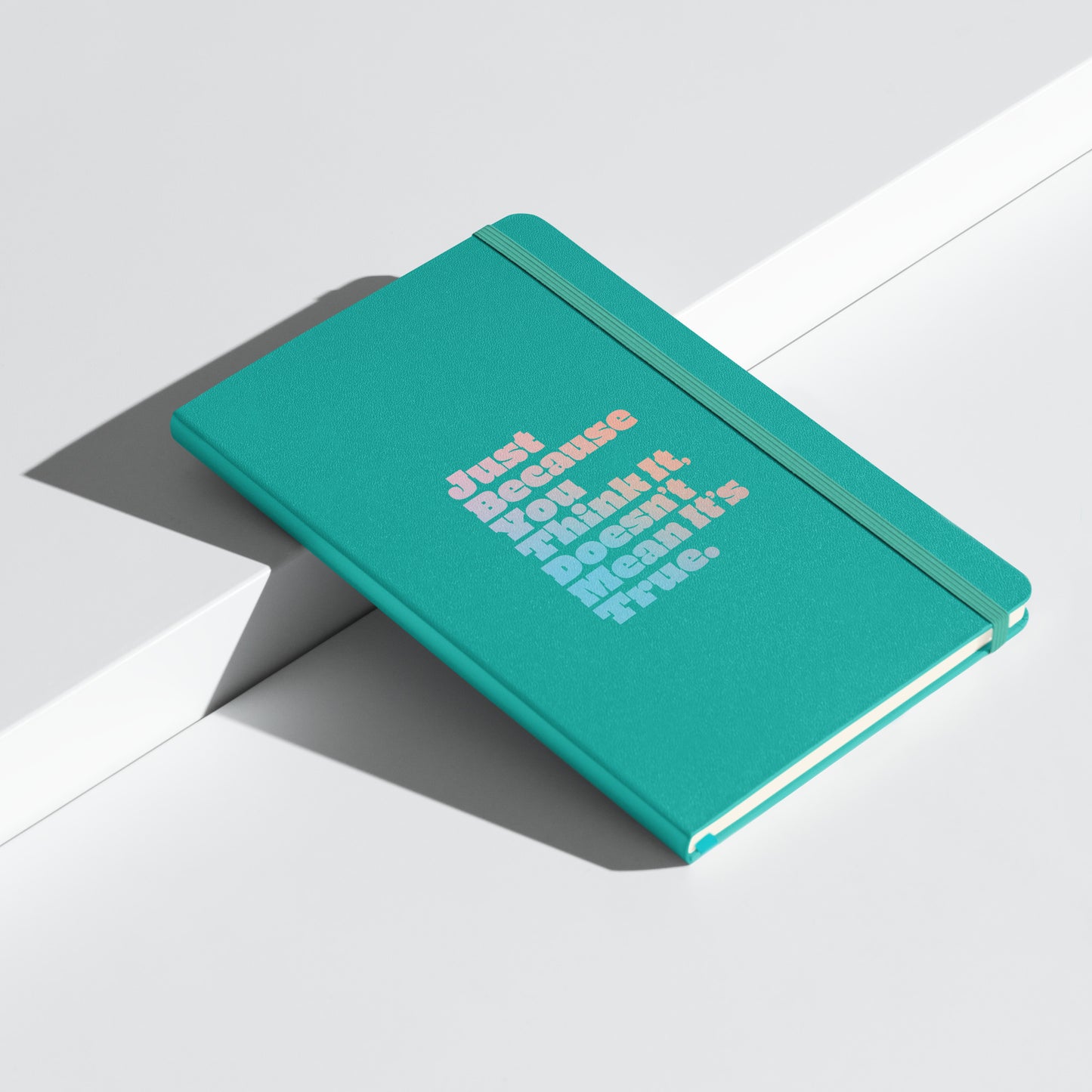 Just Because You Think It, Doesn't Mean It's True type on turquoise notebook, front angled view on white background